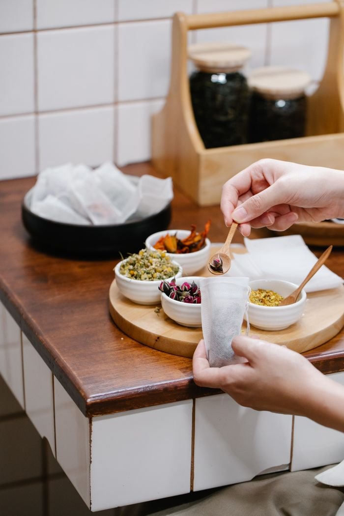 Close-up of hands preparing herbal tea with assorted dried herbs in a cozy kitchen.